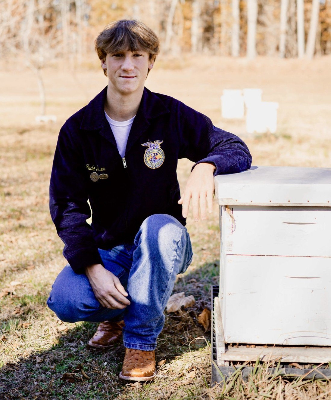 Jude in his FFA jacket, kneeling beside one of his beehives